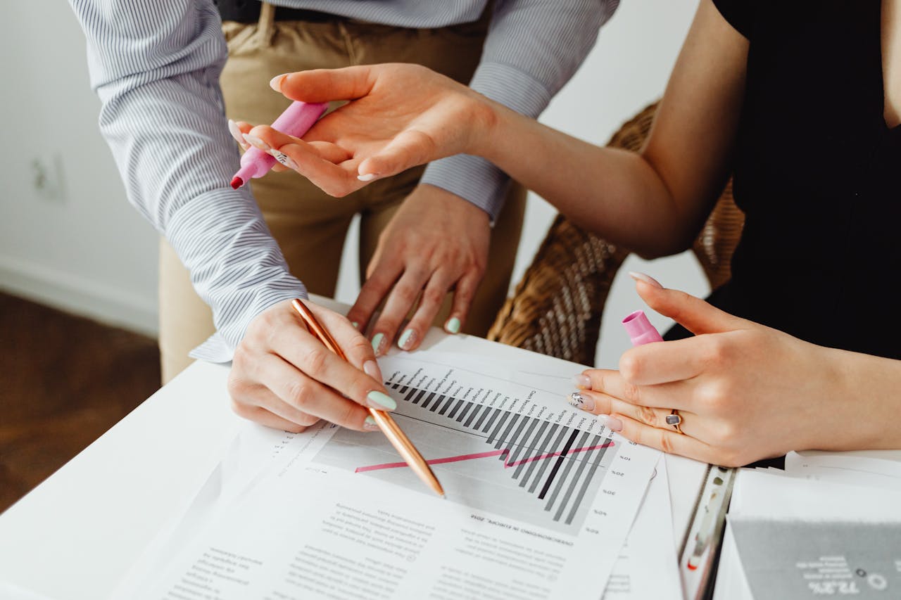 Two individuals collaborating on business chart analysis with markers in an office setting.
